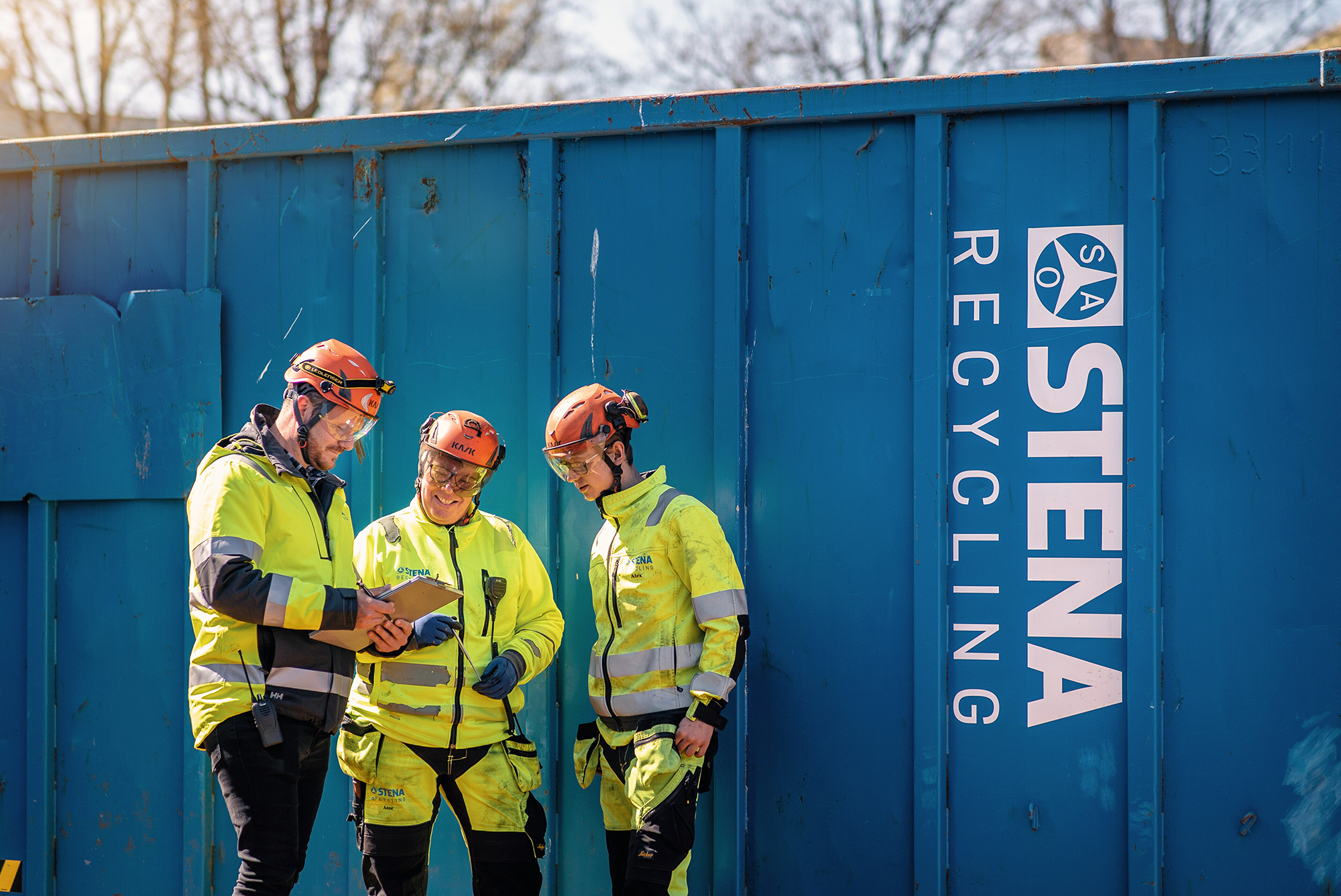 Tre medarbetare i varselkläder framför blå Stena-container