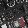 Various computer hardware components, including a graphics card, cooling fans, motherboard, hard drive, and RAM, arranged on a black surface.