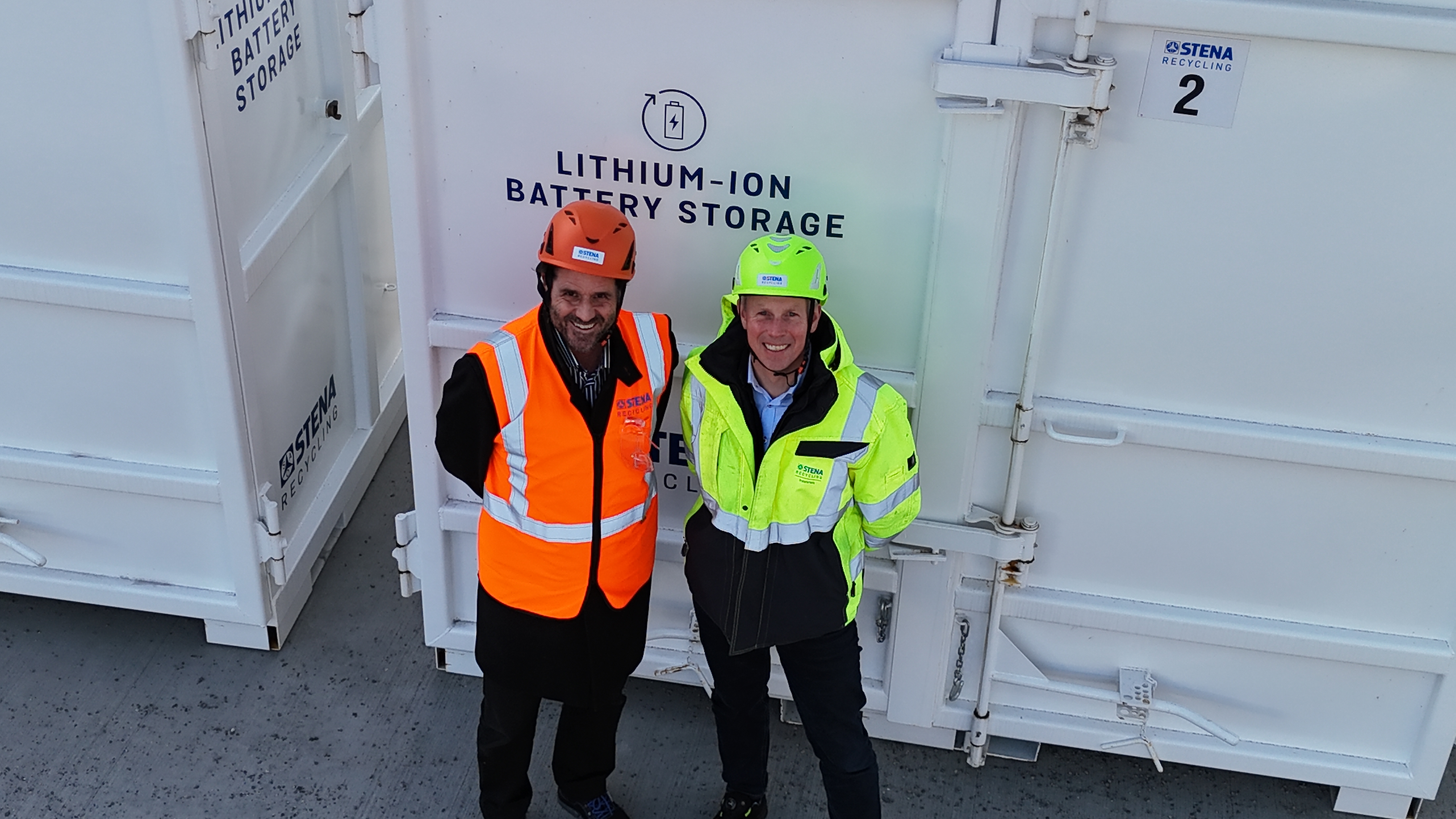 To menn iført sikkerhetsvester står ved siden av en stor batterikontainer.