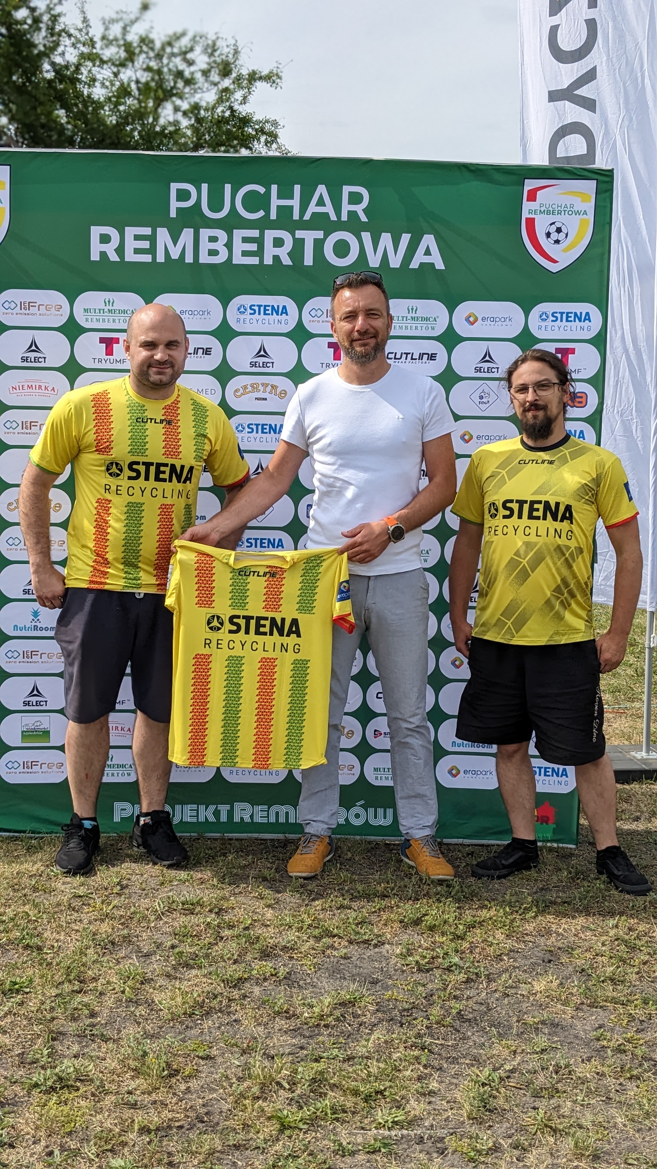 Trzy osoby na tle ścianki z logo Stena, trzymające koszulkę