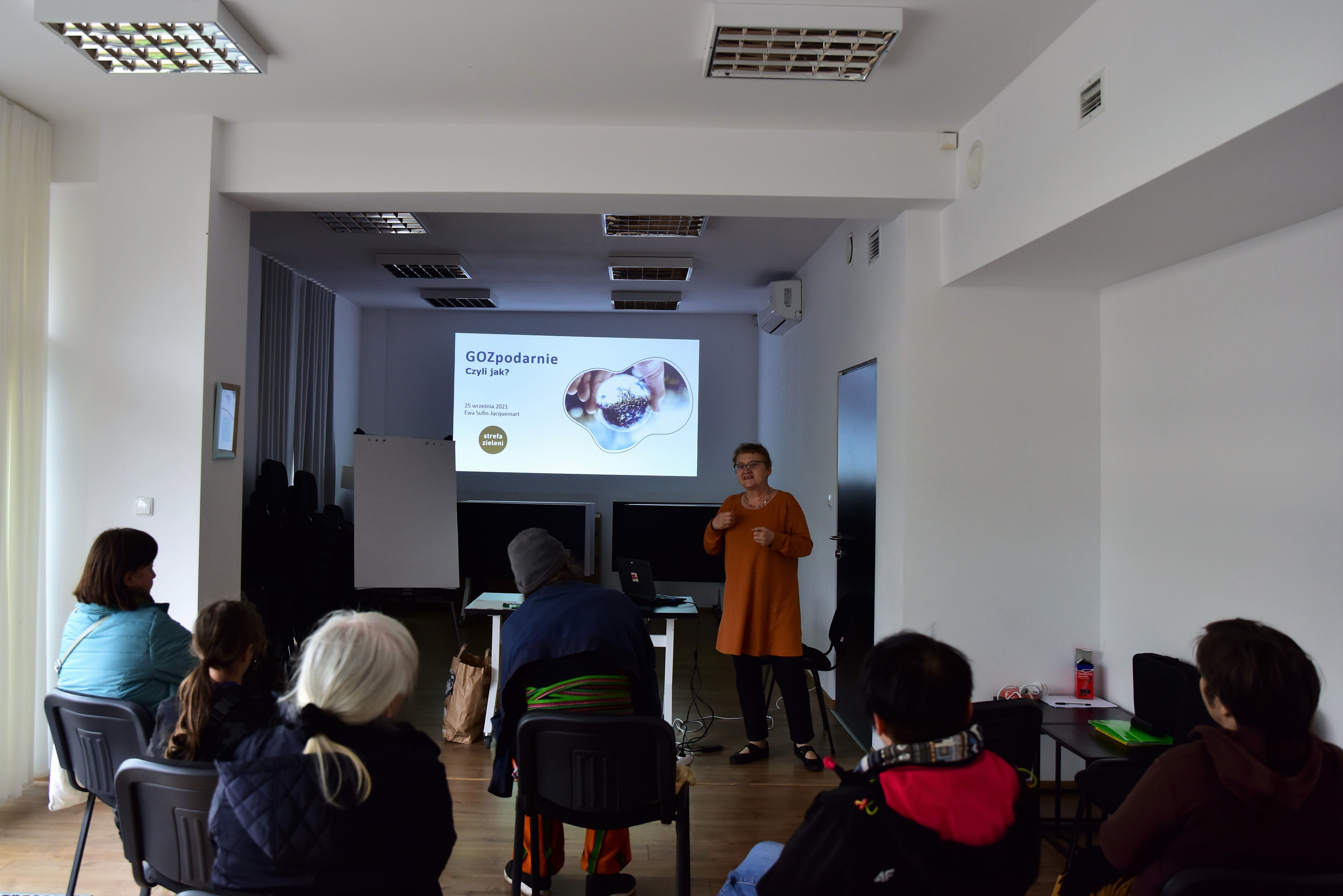 Zdjęcie pokazuje monitor, na którym wyświetlane są informacje na temat gospodarki cyrkularnej, można dostrzec dużo ludzi siedzących tyłem