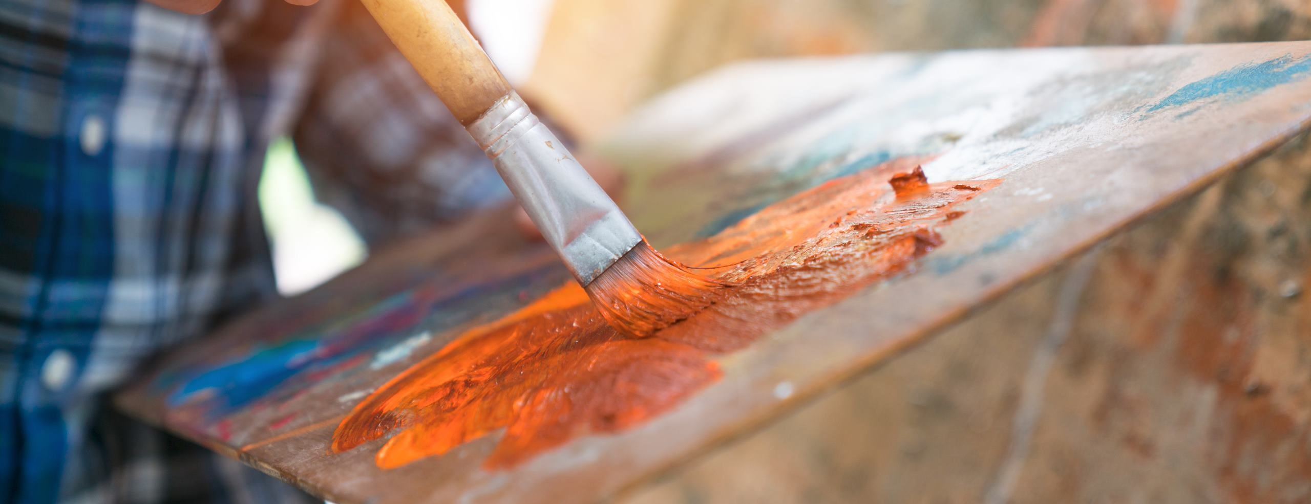 Osoba trzymająca sztalugę, na której widzimy pomarańczową farbę. W drugiej dłoni trzyma pędzel.