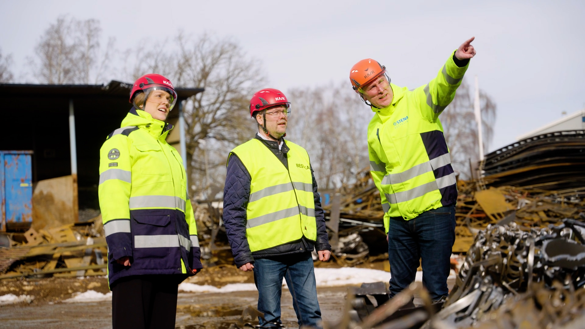 Tre personer i varsel kläder och hjälm ute på återvinningsanläggning
