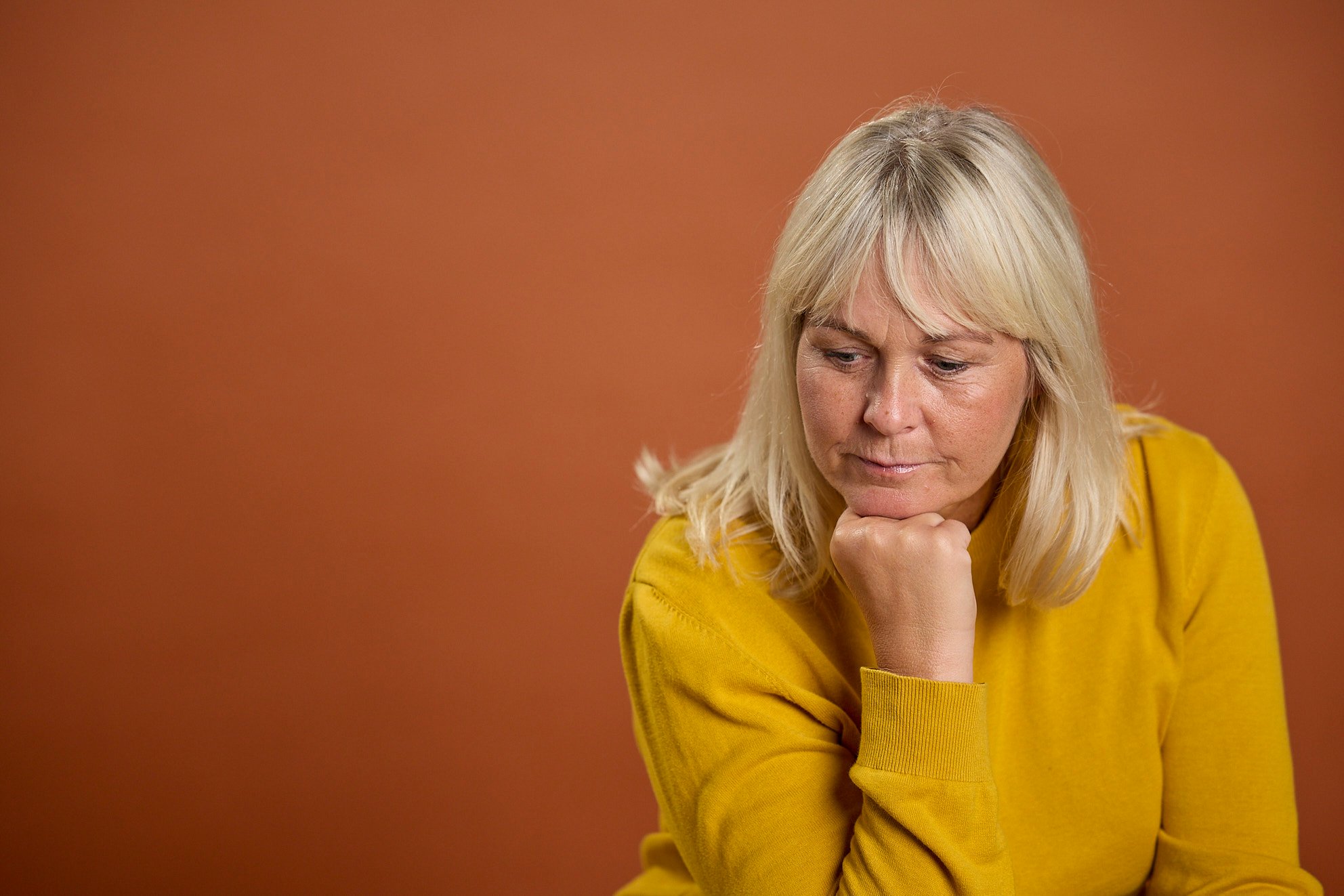 Nainen keltaisessa paidassa oranssia taustaa vasten, joka näyttää epäilevältä.