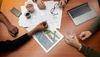 Close-up of desk covered with blueprints under the hands of two people doing planning work.