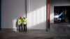 Two male Stena Recycling employees in protective gear look at a mobile phone together in a recycling facility.