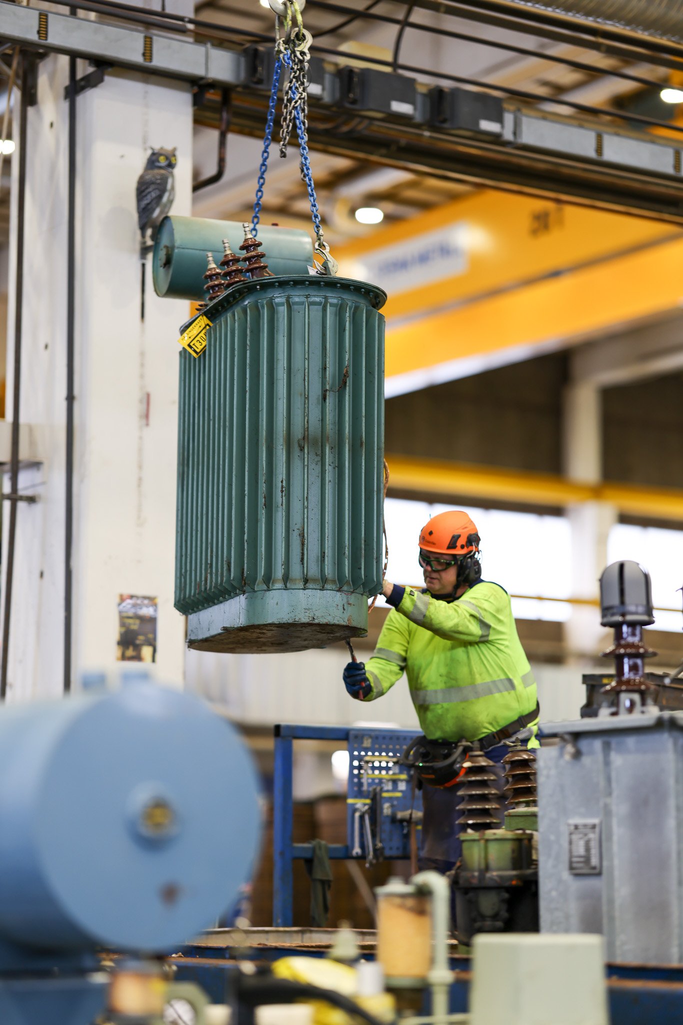 Kran som lyfter transformator och man i varselkläder jobbar