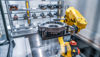 Gul industrirobotarm som løfter et arbeidsstykke i støpt metall