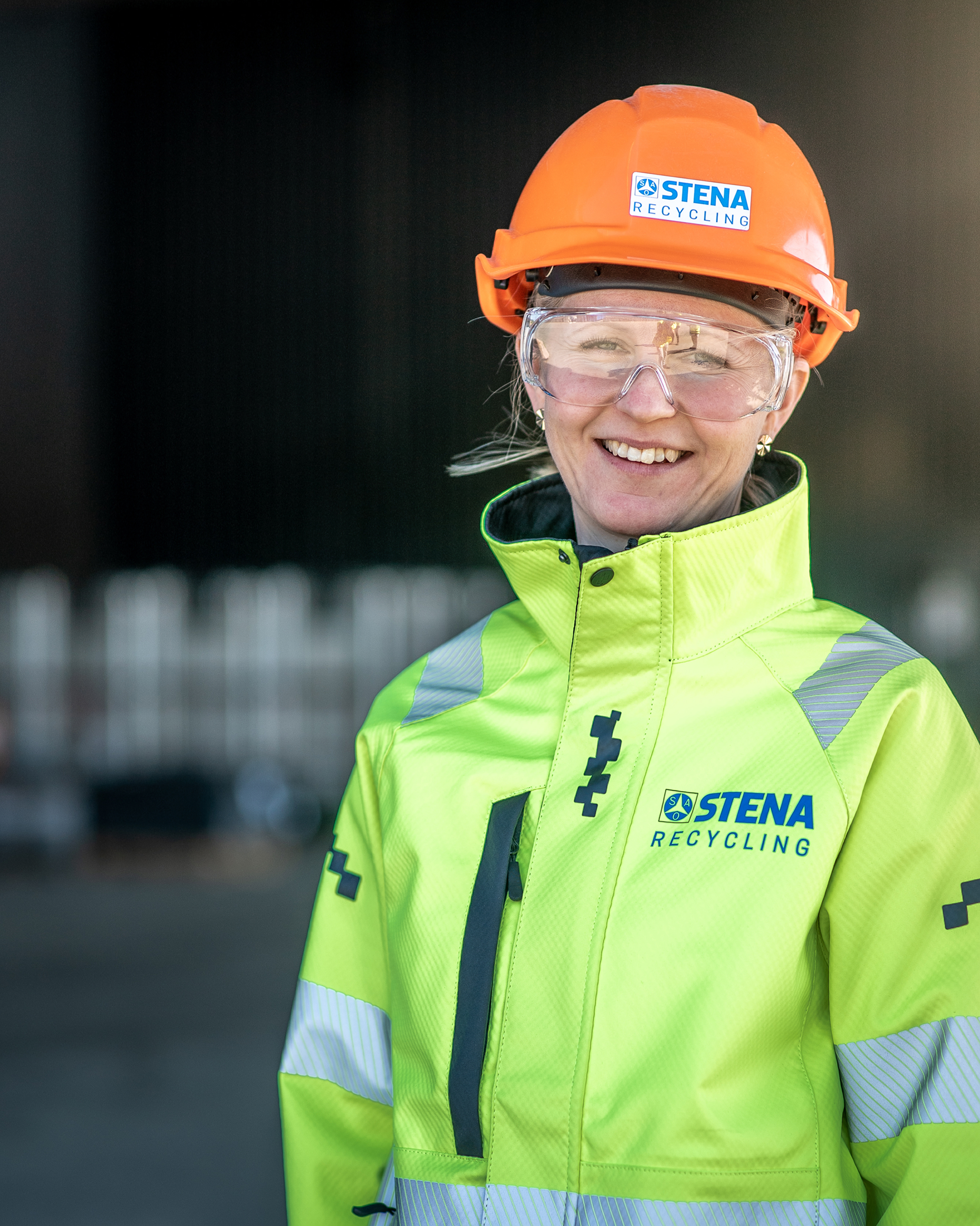 Female recycling expert looking into the camera, dressed in a reflective work jacket and hardhat