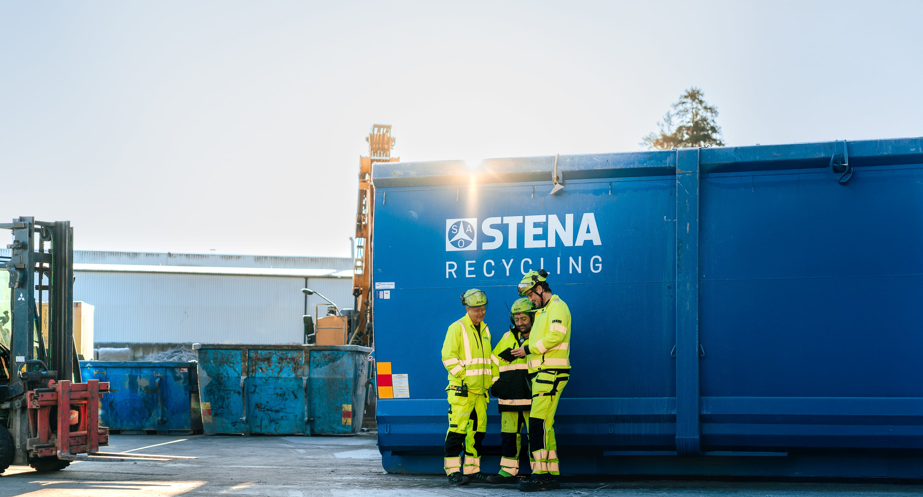 Tre personer i varselkläder som står vid en container