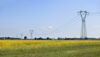 Landskap med kraftledningsstolpar som sträcker sig över ett gult rapsfält under en blå himmel