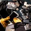 En Stena Recycling-ekspert iført beskyttelseshandsker sorterer en container med brugte mobiltelefoner. 