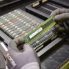 Gloved hands holding a computer memory module above a tray of electronic components for recycling and reuse.