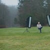 A man sitting in a chair in a field with studio lights.