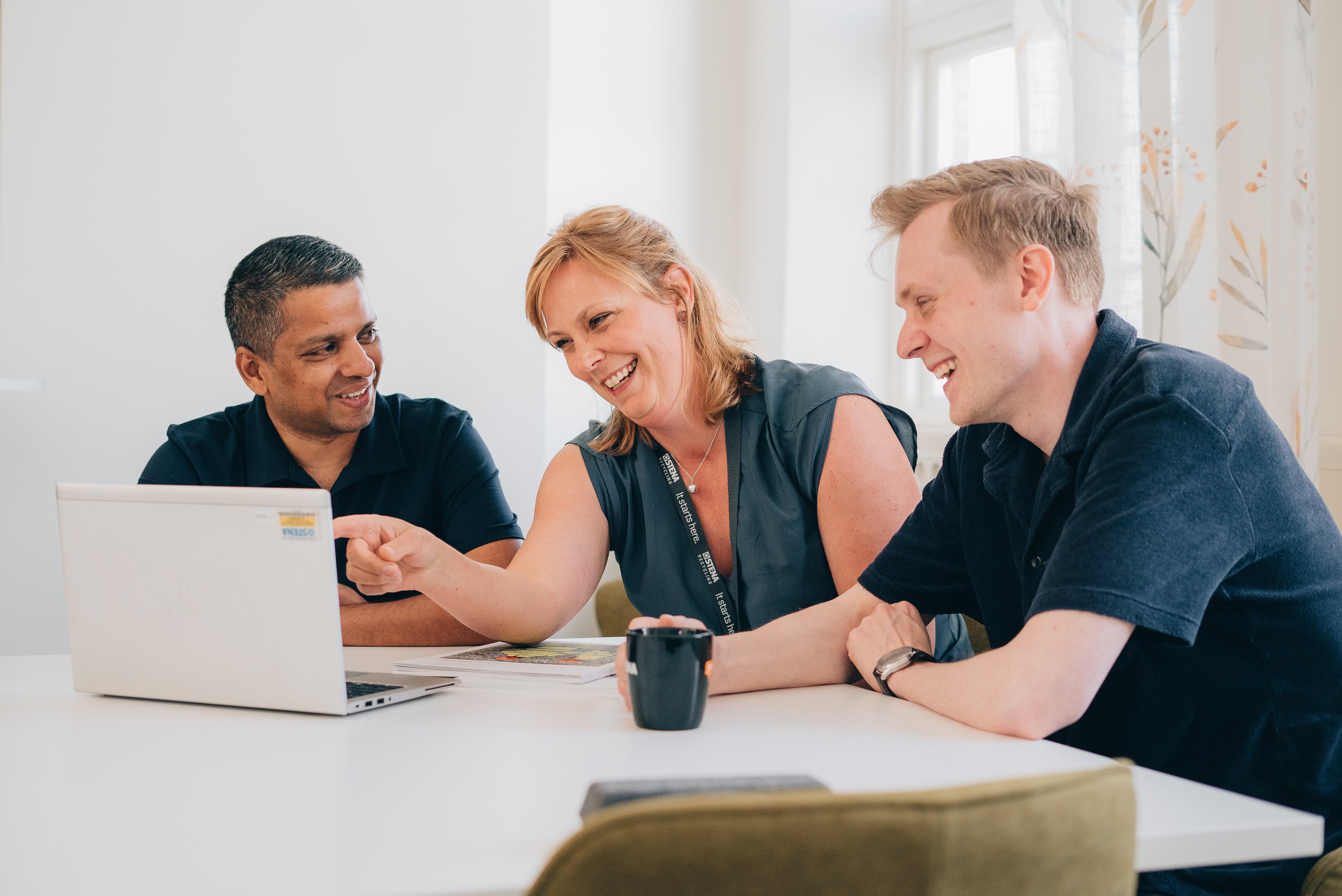 Tre personer som tittar på en laptop och skrattar