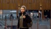 A young woman standing in a shopping centre stares directly into the camera.