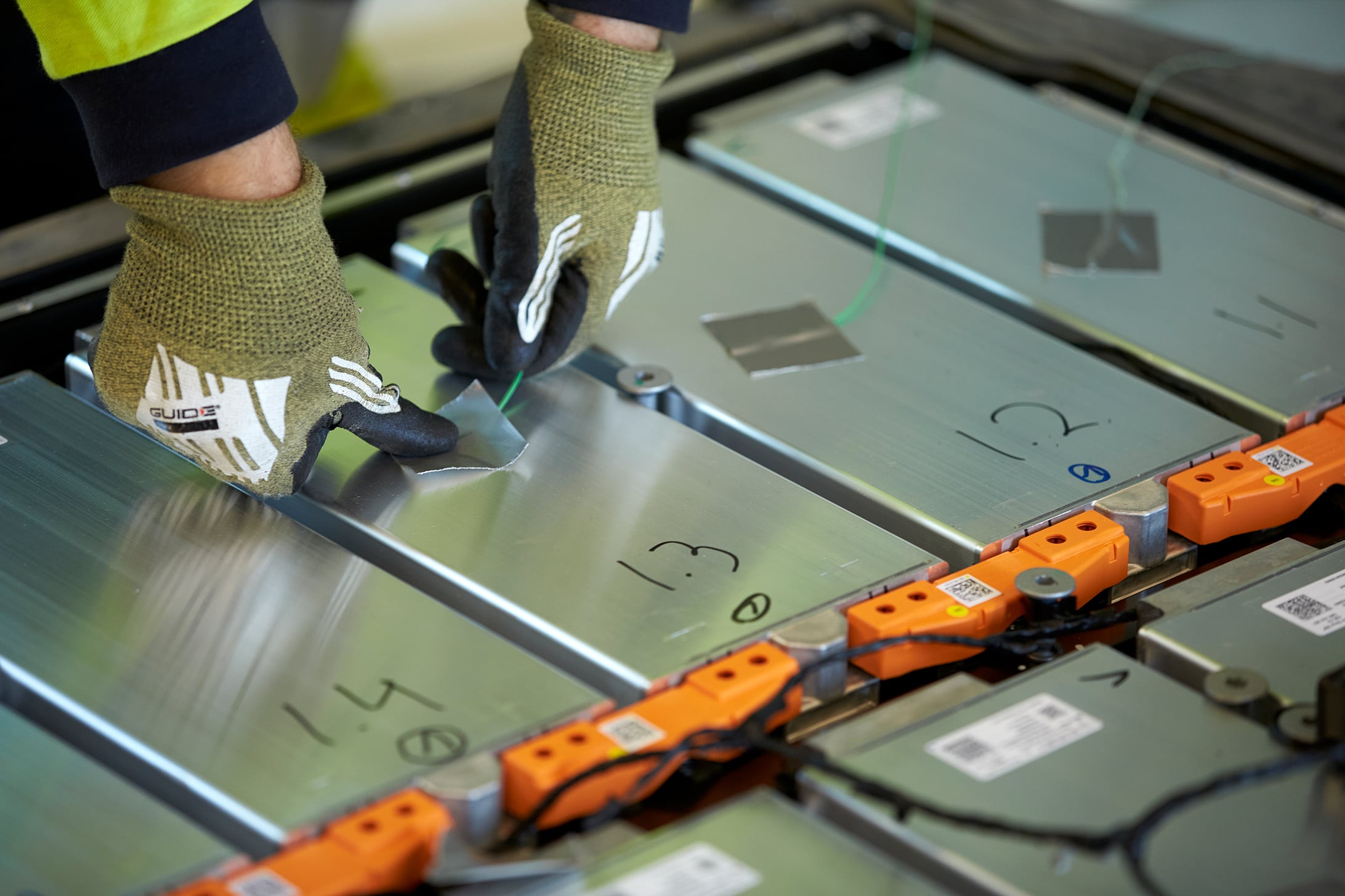 Close-up of gloved hands working on electric vehicle battery modules during inspection or recycling process
