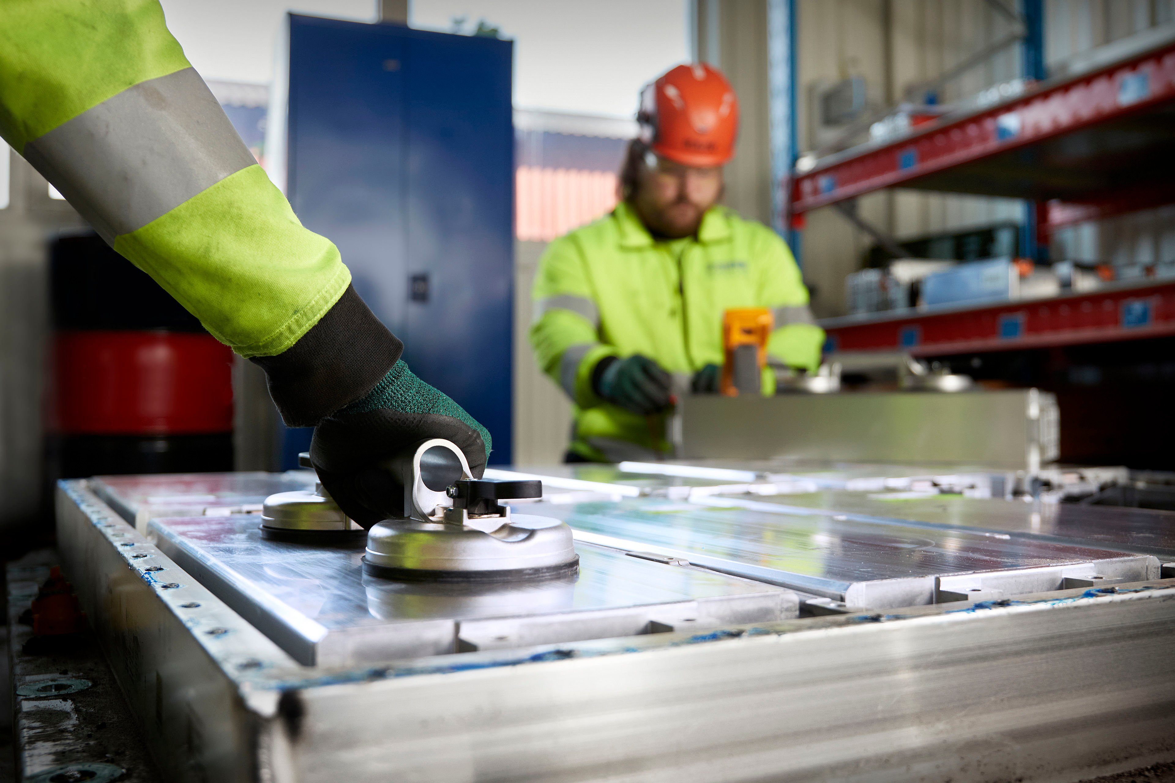 To Stena Recycling experts in protective clothing work on discahrging and dismantling a lithium-ion vehicle battery.