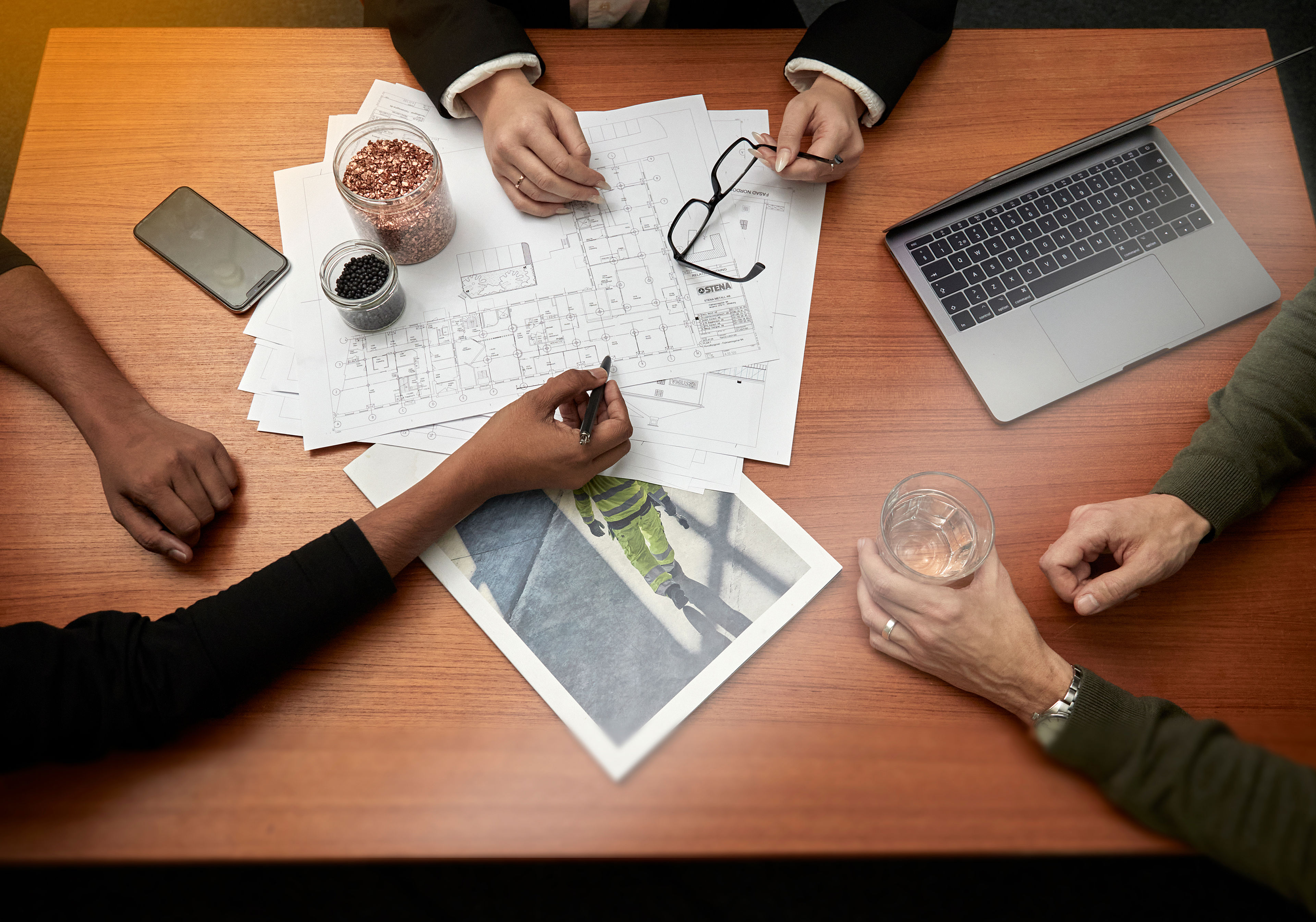 Close-up of desk covered with blueprints under the hands of two people doing planning work.