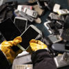 En Stena Recycling-expert som bär skyddshandskar sorterar en container med använda mobiltelefoner 